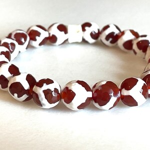 May include: A brown and white agate stone bracelet with a stretchy cord. The beads are round and have a mottled pattern.