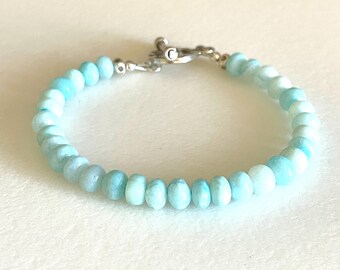May include: A light blue gemstone bracelet with a silver clasp. The bracelet is made of small, round beads.