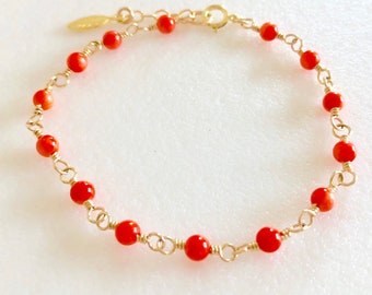 Puede incluir: Un delicado brazalete de cadena dorada con pequeñas cuentas de coral rojo brillante. El brazalete tiene un cierre simple.