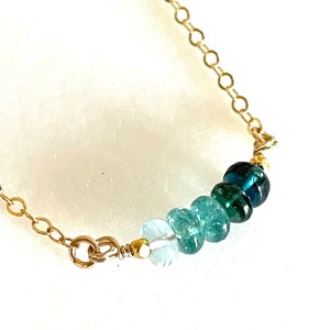 May include: A gold chain necklace with a graduated row of blue and green gemstone beads.