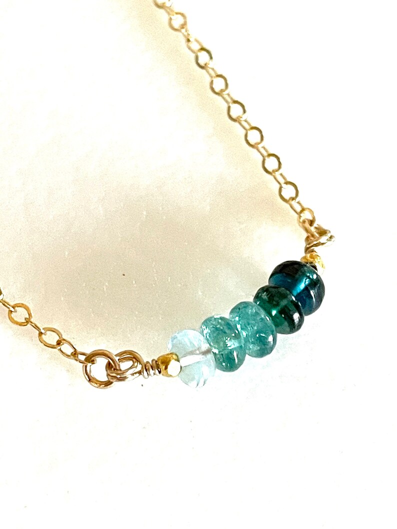 May include: A gold chain necklace with a graduated row of blue and green gemstone beads.