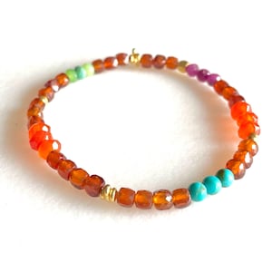 May include: A colorful beaded bracelet with orange, red, green, and turquoise beads. The bracelet is made with small, faceted beads and has a gold clasp.