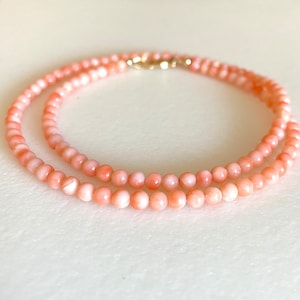 May include: A delicate necklace made of pink coral beads. The necklace is double-stranded and features a gold clasp.