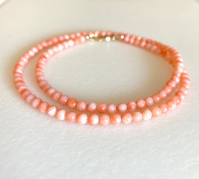 May include: A delicate necklace made of pink coral beads. The necklace is double-stranded and features a gold clasp.