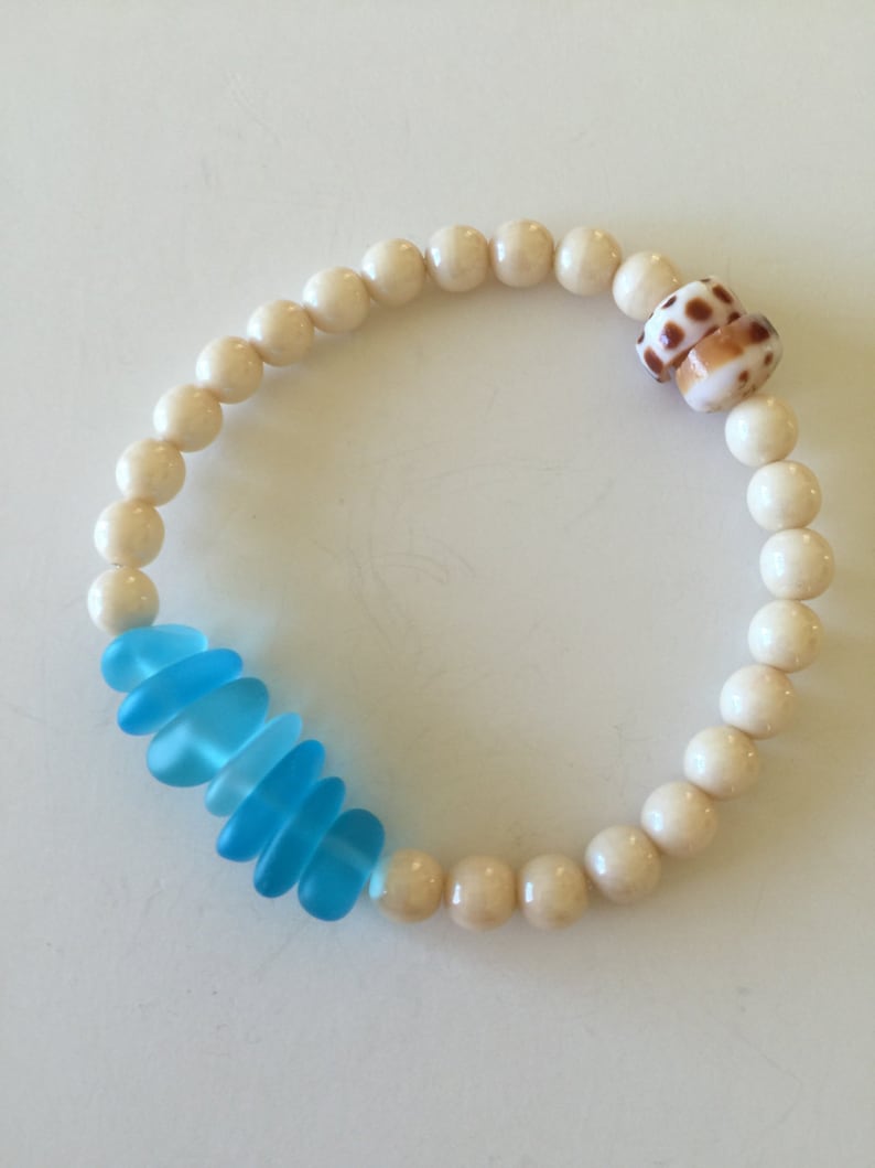May include: A white bead bracelet with a blue glass accent and a brown and white seashell charm.