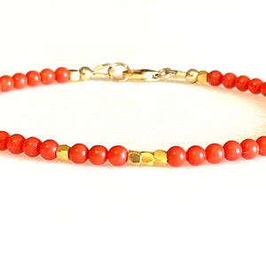 Pode incluir: Uma pulseira delicada com pequenas contas redondas cor de coral, intercaladas com contas geom&eacute;tricas douradas. A pulseira &eacute; presa com um fecho dourado. O design geral &eacute; simples e elegante.