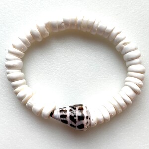 K&ouml;nnte beinhalten: Armband aus wei&szlig;en Muschelkernperlen mit einem einzigen braunen und wei&szlig;en Muschel-Anh&auml;nger.
