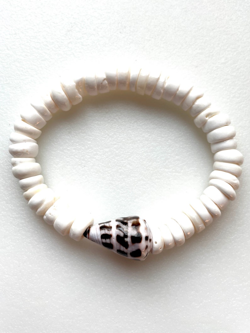 K&ouml;nnte beinhalten: Armband aus wei&szlig;en Muschelkernperlen mit einem einzigen braunen und wei&szlig;en Muschel-Anh&auml;nger.