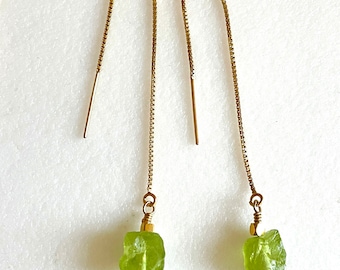 May include: A pair of gold chain earrings with green gemstone drops. The gemstones are rough and have a natural, unpolished look.
