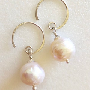 May include: A pair of silver hoop earrings with a white pearl dangling from each hoop.