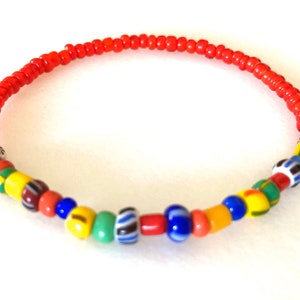 Könnte beinhalten: Ein rotes Perlenarmband mit einem bunten Streifen aus Perlen in der Mitte. Der Streifen enthält gelbe, grüne, blaue, rote und weiße Perlen.