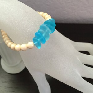 May include: A bracelet with white wooden beads and a row of light blue glass beads.