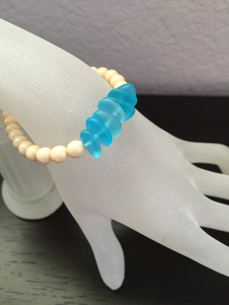 May include: A bracelet with white wooden beads and a row of light blue glass beads.