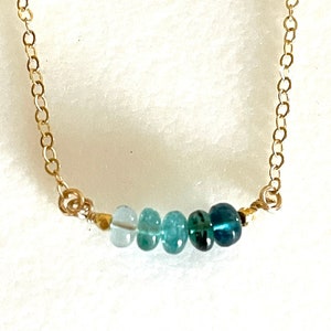 May include: A delicate gold chain necklace with a graduated row of light blue to dark blue gemstone beads.