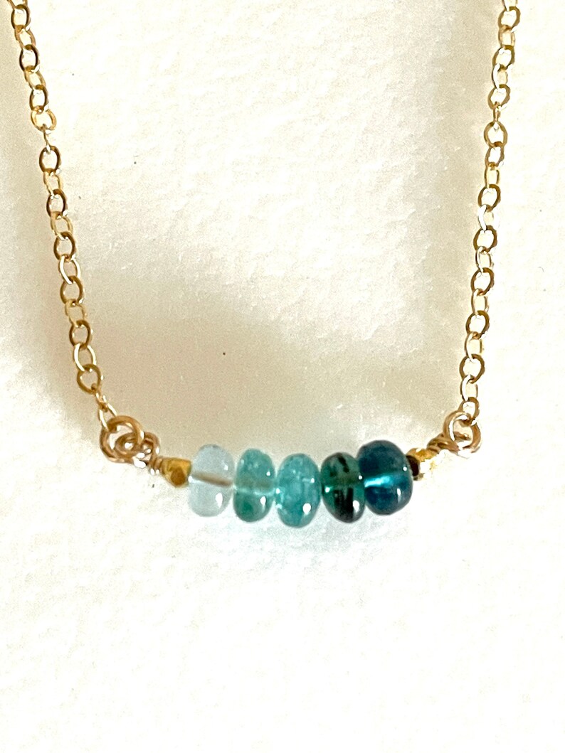 May include: A delicate gold chain necklace with a graduated row of light blue to dark blue gemstone beads.