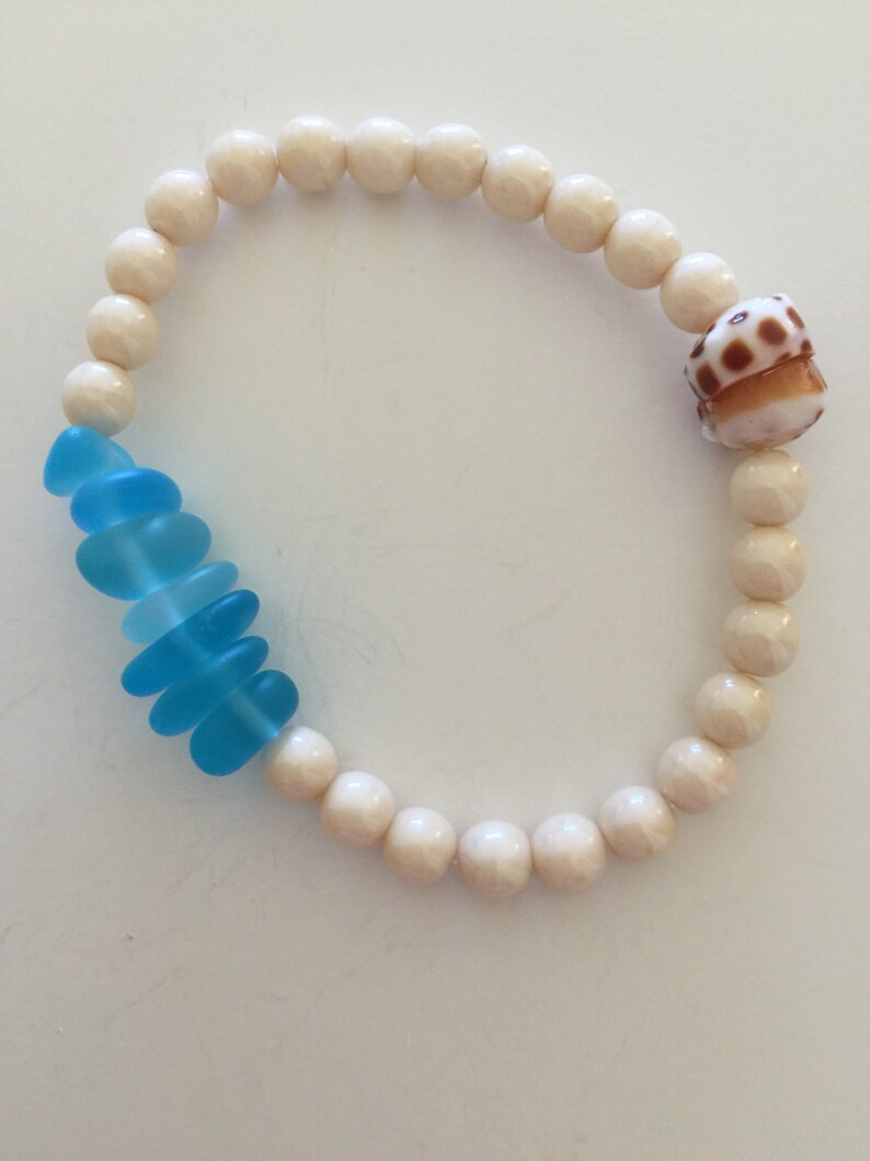 May include: A white beaded bracelet with a blue glass charm and a brown seashell charm.