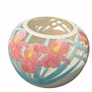 May include: A spherical ceramic bowl featuring an openwork lattice design in light blue. The exterior is decorated with raised, hand-painted pink iris flowers with yellow centers. The bowl has a smooth, white interior and a wide circular opening.