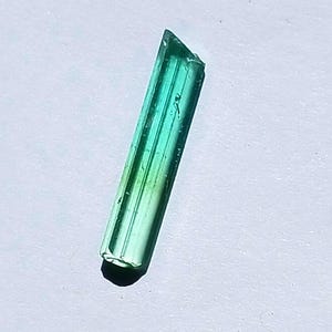 Op de afbeelding: Een groen en blauw edelsteenkristal met een puntige punt en een platte basis.