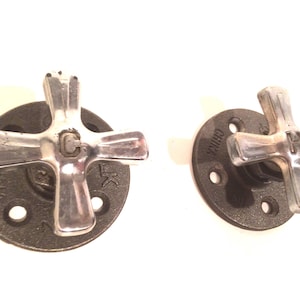 May include: Two black metal pipe flanges with silver cross-shaped handles. The flanges have the words "CHINK" and "LK" printed on them.