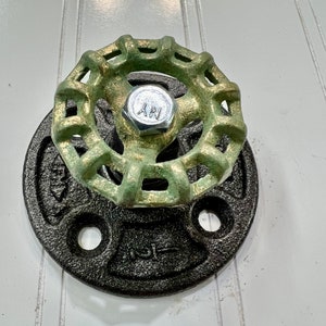 May include: A green metal valve with a black metal base. The valve has a decorative design and is attached to a black metal flange.