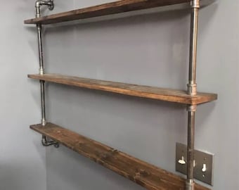 May include: Three-tiered industrial-style shelf unit with dark brown wooden shelves and silver metal pipes. The shelves are mounted to a gray wall.