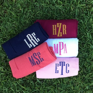 May include: Five waffle weave towels with different embroidered initials. The towels are in the colors navy blue, burgundy, coral, pink, and white.