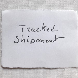 Puede incluir: Una nota escrita a mano en un papel blanco que dice "Tracked Shipment".