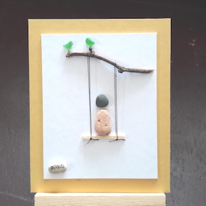 Kind auf einer Schaukel, poetische Komposition aus poliertem Glas und Kieselsteinen, Wanddekoration, Seeglaskunst. Seeglas-Postkarte