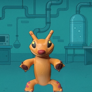 May include: Orange figurine of a cartoon creature with large eyes, a red nose, and pink accents on its feet and hands. The figure is posed with arms outstretched. The background is a teal-colored laboratory setting.