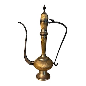May include: A vintage brass pitcher with a long, curved spout and a black handle. The pitcher has intricate etched designs and a bulbous body. The overall color is gold with darker accents, suggesting age and use. The pitcher is likely decorative.