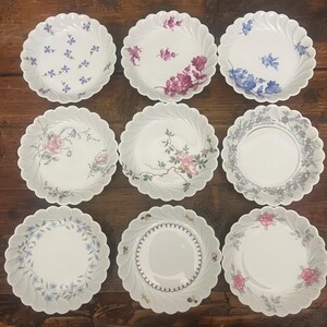 Pode incluir: Uma cole&ccedil;&atilde;o de nove pratos de porcelana branca dispostos numa grelha de tr&ecirc;s por tr&ecirc;s. Cada prato apresenta uma borda recortada e um padr&atilde;o floral &uacute;nico, incluindo ramos azuis, rosas cor-de-rosa e bordas decorativas cinzentas ou douradas.