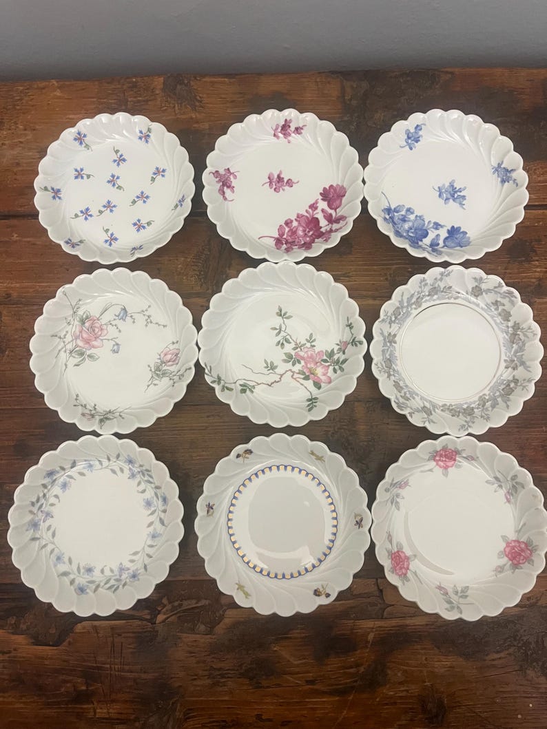 Pode incluir: Uma cole&ccedil;&atilde;o de nove pratos de porcelana branca dispostos numa grelha de tr&ecirc;s por tr&ecirc;s. Cada prato apresenta uma borda recortada e um padr&atilde;o floral &uacute;nico, incluindo ramos azuis, rosas cor-de-rosa e bordas decorativas cinzentas ou douradas.