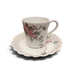 Pode incluir: Um conjunto de ch&aacute;vena e pires em porcelana branca com o texto Julia by Haviland. A ch&aacute;vena e o pires t&ecirc;m uma textura canelada em espiral e est&atilde;o decorados com um padr&atilde;o delicado de flores cor-de-rosa, folhas verdes e ramos castanhos.
