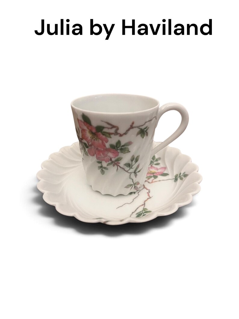 Pode incluir: Um conjunto de ch&aacute;vena e pires em porcelana branca com o texto Julia by Haviland. A ch&aacute;vena e o pires t&ecirc;m uma textura canelada em espiral e est&atilde;o decorados com um padr&atilde;o delicado de flores cor-de-rosa, folhas verdes e ramos castanhos.