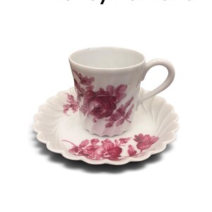 Pode incluir: Um conjunto de ch&aacute;vena e pires em porcelana branca com um padr&atilde;o floral rosa escuro. A ch&aacute;vena tem uma asa curva e um corpo canelado, enquanto o pires apresenta uma borda recortada. O texto H4491 by Haviland est&aacute; impresso acima do conjunto.