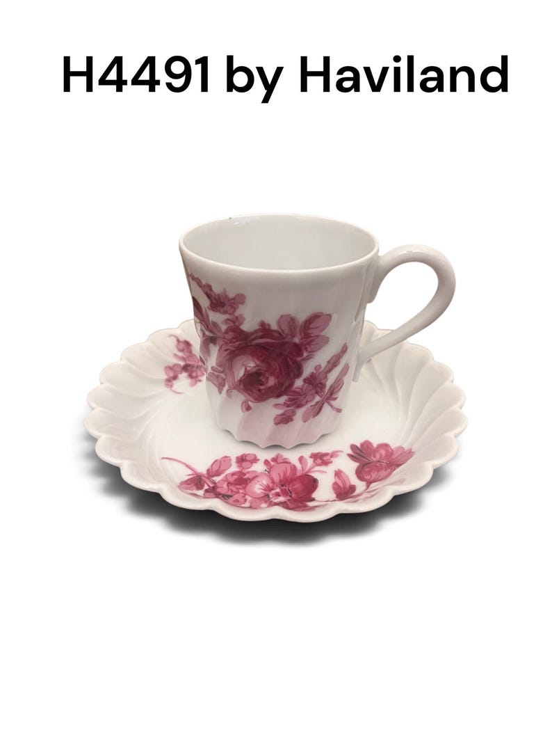 Pode incluir: Um conjunto de ch&aacute;vena e pires em porcelana branca com um padr&atilde;o floral rosa escuro. A ch&aacute;vena tem uma asa curva e um corpo canelado, enquanto o pires apresenta uma borda recortada. O texto H4491 by Haviland est&aacute; impresso acima do conjunto.