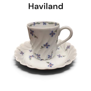 Pode incluir: Um conjunto de ch&aacute;vena e pires de porcelana branca da Haviland, com uma textura canelada em espiral e um padr&atilde;o delicado de cent&aacute;ureas azuis com caules verdes. O texto Cornflower by Haviland &eacute; exibido acima da ch&aacute;vena e do pires.