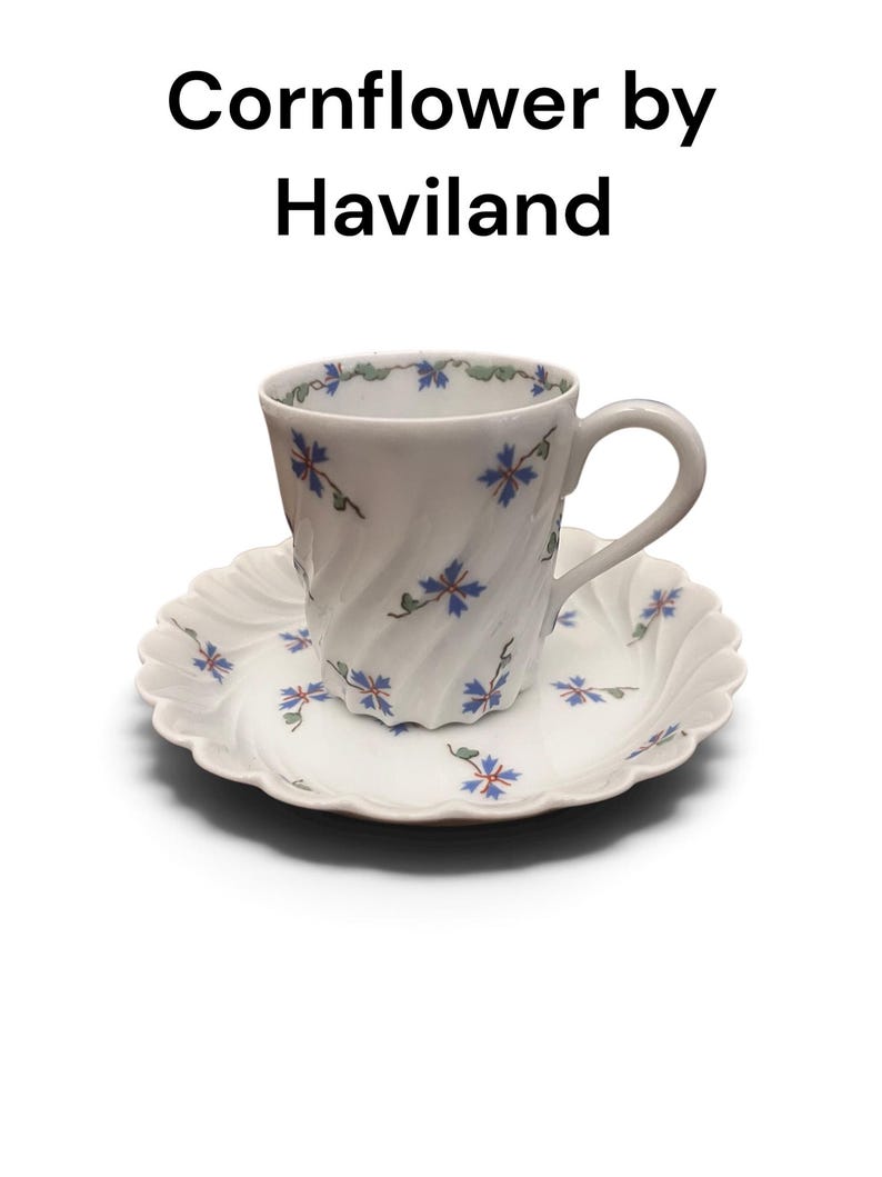 Pode incluir: Um conjunto de ch&aacute;vena e pires de porcelana branca da Haviland, com uma textura canelada em espiral e um padr&atilde;o delicado de cent&aacute;ureas azuis com caules verdes. O texto Cornflower by Haviland &eacute; exibido acima da ch&aacute;vena e do pires.