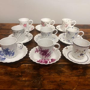 Pode incluir: Um conjunto de oito ch&aacute;venas de ch&aacute; em porcelana branca com pires a condizer, cada uma com um padr&atilde;o floral &uacute;nico em cores como azul, roxo, rosa e verde. As ch&aacute;venas t&ecirc;m uma textura canelada em espiral e bordos recortados.