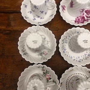 Pode incluir: Seis ch&aacute;venas de ch&aacute; e pires em porcelana branca dispostos em duas colunas. Cada pe&ccedil;a apresenta uma borda recortada e um padr&atilde;o em espiral. As ch&aacute;venas est&atilde;o invertidas, exibindo o selo Haviland France Limoges. Motivos florais decoram o conjunto.