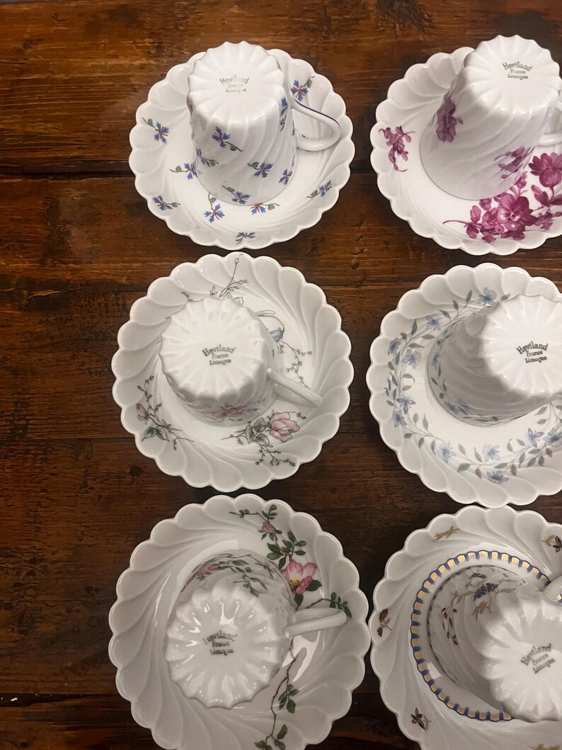 Pode incluir: Seis ch&aacute;venas de ch&aacute; e pires em porcelana branca dispostos em duas colunas. Cada pe&ccedil;a apresenta uma borda recortada e um padr&atilde;o em espiral. As ch&aacute;venas est&atilde;o invertidas, exibindo o selo Haviland France Limoges. Motivos florais decoram o conjunto.