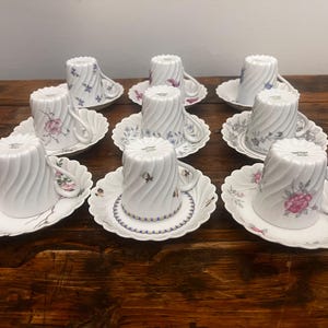 Pode incluir: Um conjunto de oito ch&aacute;venas de ch&aacute; e pires em porcelana branca dispostos em tr&ecirc;s filas. Cada ch&aacute;vena apresenta um padr&atilde;o de espiral vertical e uma asa. As ch&aacute;venas e os pires est&atilde;o decorados com v&aacute;rios motivos florais delicados.