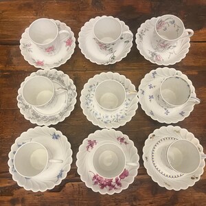 Pode incluir: Um conjunto de nove ch&aacute;venas de ch&aacute; em porcelana branca com pires recortados a condizer, dispostos numa grelha. Cada conjunto apresenta um padr&atilde;o floral ou bot&acirc;nico &uacute;nico em v&aacute;rias cores, incluindo rosa, azul, roxo e cinzento.