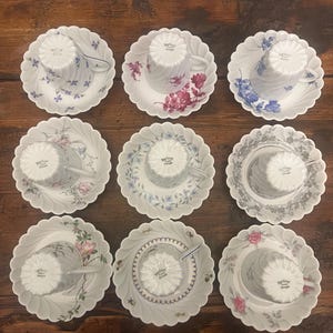Pode incluir: Um conjunto de nove ch&aacute;venas de ch&aacute; e pires em porcelana branca dispostos numa grelha. Cada pe&ccedil;a apresenta uma borda recortada e um padr&atilde;o floral ou bot&acirc;nico &uacute;nico em v&aacute;rias cores, incluindo azul, rosa, vermelho e cinzento.
