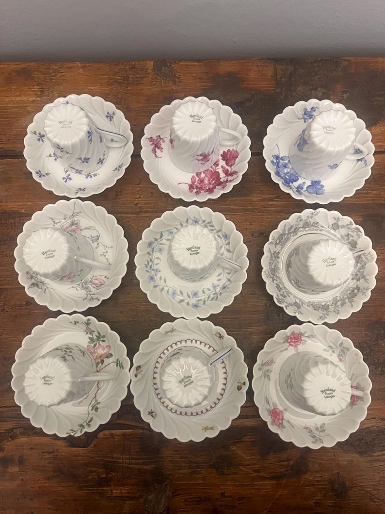Pode incluir: Um conjunto de nove ch&aacute;venas de ch&aacute; e pires em porcelana branca dispostos numa grelha. Cada pe&ccedil;a apresenta uma borda recortada e um padr&atilde;o floral ou bot&acirc;nico &uacute;nico em v&aacute;rias cores, incluindo azul, rosa, vermelho e cinzento.