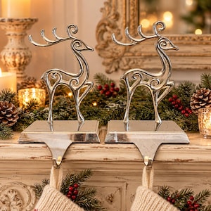 May include: A pair of silver-toned metal stocking holders, each featuring a stylized reindeer silhouette with curved antlers. The reindeer figures are mounted on rectangular bases, with a hook extending downward to support a stocking.