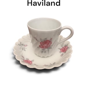 Pode incluir: Um conjunto de ch&aacute;vena e pires em porcelana branca Sylvia White by Haviland com um delicado padr&atilde;o floral de rosas cor-de-rosa e folhas verdes. A ch&aacute;vena tem uma textura espiralada e o texto Sylvia White by Haviland est&aacute; presente.
