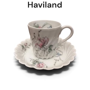 Pode incluir: Um conjunto de ch&aacute;vena e pires de porcelana branca da Haviland no padr&atilde;o Eglantine. A ch&aacute;vena apresenta um corpo canelado em espiral com ilustra&ccedil;&otilde;es de rosas cor-de-rosa e folhas verdes. O pires tem uma borda recortada e motivos florais.