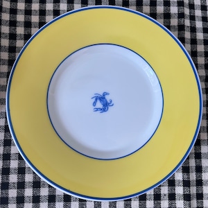 May include: A yellow and blue ceramic plate with a blue crab design in the center. The plate has a wide yellow rim with a thin blue border.