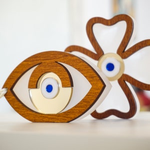 May include: Two wooden evil eye charms, one shaped like an eye and the other like a flower. Both charms have a blue and white evil eye in the center.